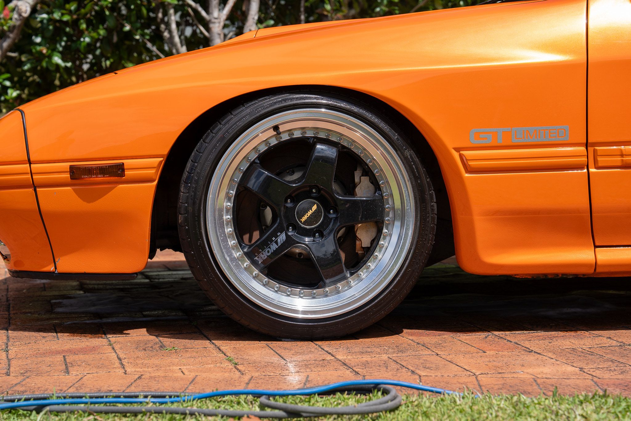 Orange Mazda RX-7 with polished deep-dish wheel, detailed on a home driveway